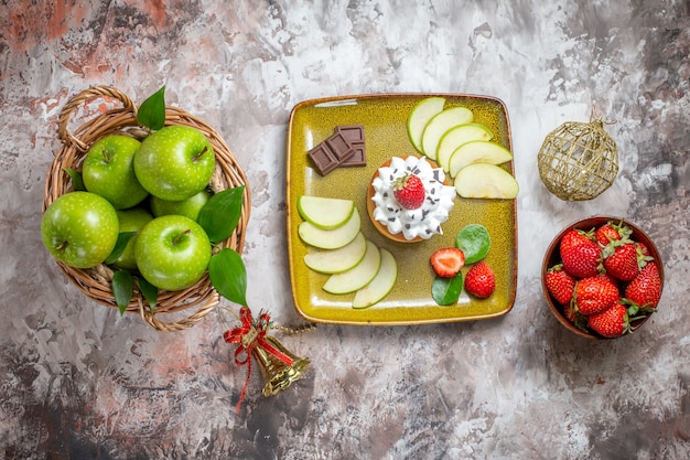 Bovenaanzicht gesneden groene appels met aardbeien en cake op lichte achtergrond