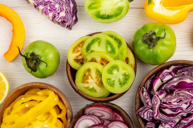 Bovenaanzicht gesneden groene tomaten gele paprika rode kool rode ui in houten kom op witte grond