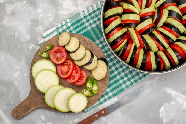 Bovenaanzicht gesneden groenten zoals tomaten en aubergines vers en gekookt op de lichte tafel rijpe verse groente maaltijd maaltijd schotel