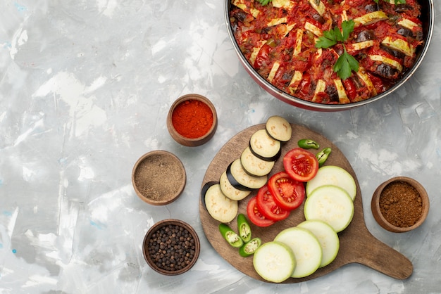 Bovenaanzicht gesneden groenten zoals tomaten en aubergines vers en gekookt op het lichte bureau rijp vers plantaardig voedsel