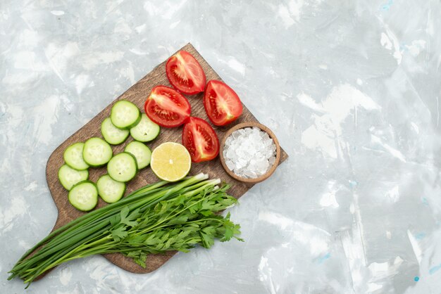 Bovenaanzicht gesneden komkommers en tomaten met zoutgreens en citroen op wit, salade plantaardig groen voedsel