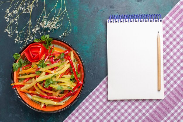 Bovenaanzicht gesneden paprika gekleurde pittige salade met blocnote op donkerblauw bureau