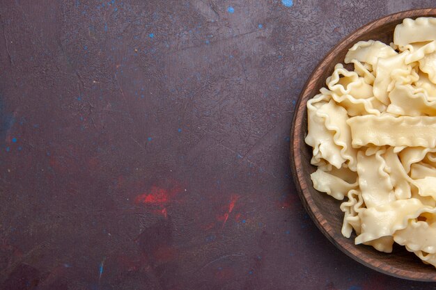 Bovenaanzicht gesneden rauw deeg binnen bruine plaat op donkere vloer maaltijd deeg eten pasta diner