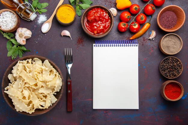 Bovenaanzicht gesneden rauw deeg met tomaten en kruiden op donkere bureau deeg pasta maaltijd voedsel groente