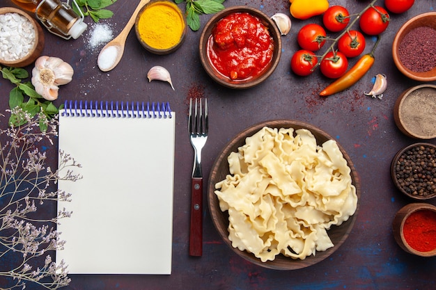 Bovenaanzicht gesneden rauw deeg met tomaten en verschillende kruiden op donkere achtergrond deeg pasta maaltijd voedsel groente