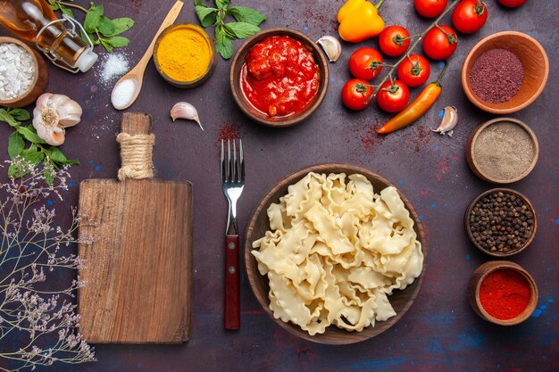 Bovenaanzicht gesneden rauw deeg met tomaten en verschillende kruiden op donkere achtergrond deeg pasta maaltijd voedsel groente