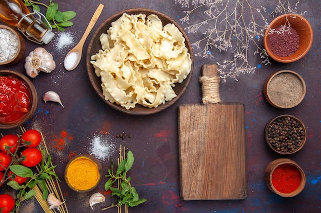 Bovenaanzicht gesneden rauw deeg met verschillende kruiderijen op donker bureau maaltijd diner pastadeeg