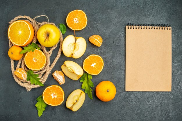 Bovenaanzicht gesneden sinaasappelen en appels een notitieblok op donkere achtergrond