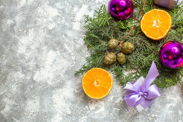 Bovenaanzicht gesneden sinaasappelen pijnboom takken kerstboom speelgoed kleine geschenken op grijze achtergrond