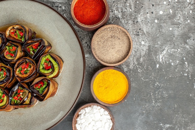 Bovenaanzicht gevulde aubergine rolt hete peper poeder kurkuma in kleine kommen op grijze achtergrond