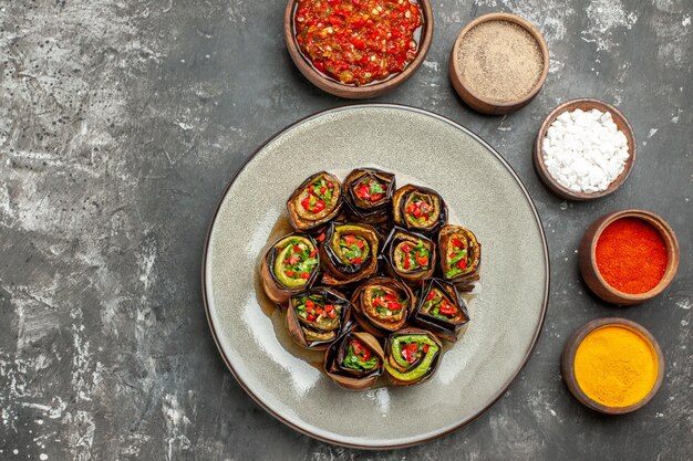 Bovenaanzicht gevulde aubergine rolt kruiden in kleine kommen zout peper rode peper kurkuma adjika op grijze ondergrond