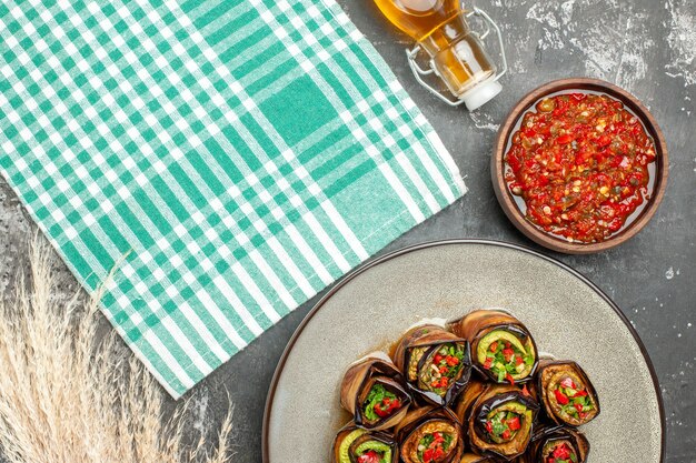 Bovenaanzicht gevulde auberginebroodjes in witte ovale plaat adjika in kleine kom turquoise-wit tafelkleed olie op grijze achtergrond