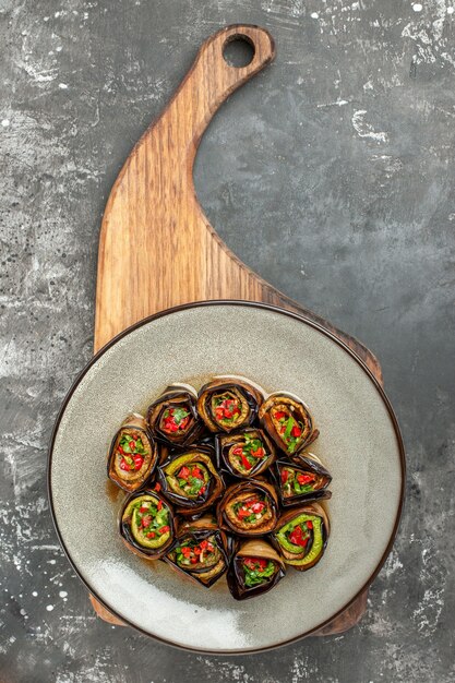 Bovenaanzicht gevulde auberginebroodjes in witte ovale plaat op houten dienblad met handvat op grijze achtergrond