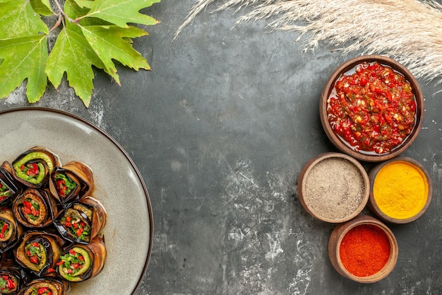 Bovenaanzicht gevulde auberginebroodjes in witte plaat verschillende kruiden in kleine kommen adjika op grijs oppervlak