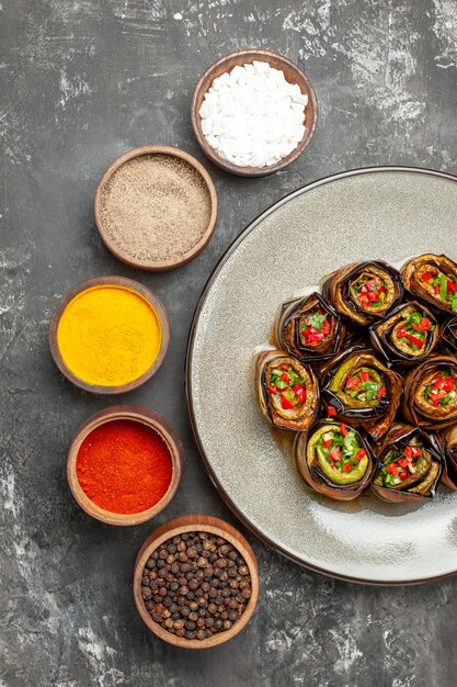 Bovenaanzicht gevulde auberginebroodjes op witte ovale plaat verschillende kruiden op grijs oppervlak