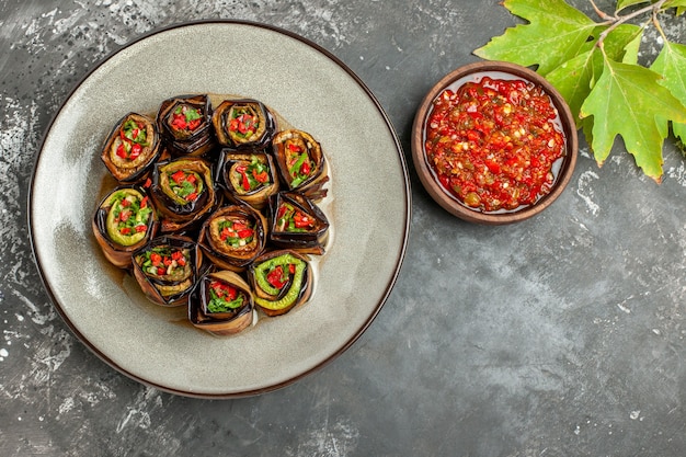 Gratis foto bovenaanzicht gevulde auberginebroodjes op witte plaat adjika vork en mes op grijze achtergrond met vrije ruimte