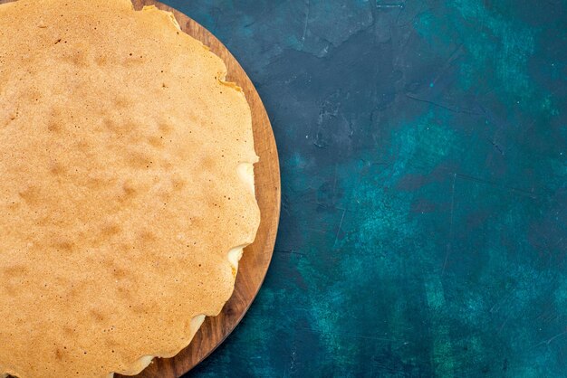 Bovenaanzicht gewoon cakedeeg gebakken rond gevormd op donkerblauw bureau