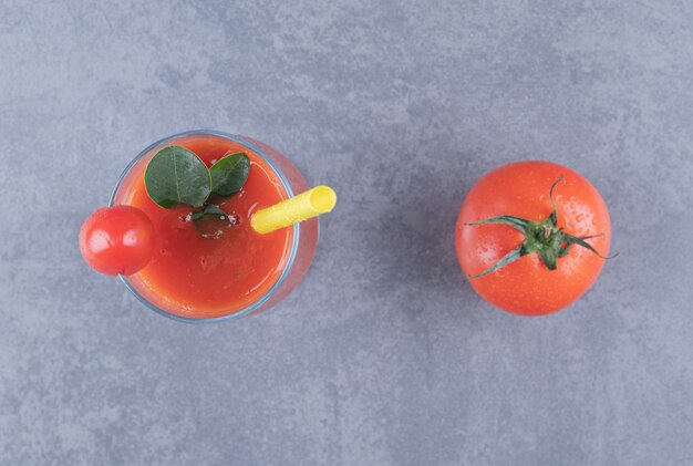 Bovenaanzicht. Glas vers tomatensap en tomaten op een grijze achtergrond.