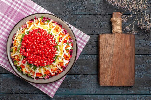 Gratis foto bovenaanzicht granaatappel citroen knoflook houten snijplank naast de boomtakken en bord smakelijk gerecht op het roze-wit geruite tafelkleed op tafel