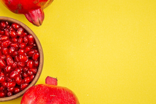 Bovenaanzicht granaatappel twee granaatappels kom met zaden van granaatappel op de gele tafel