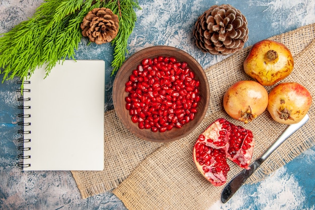 Bovenaanzicht granaatappel zaden in houten kom diner mes granaatappels notebook pijnboomtak en kegels op blauw-wit oppervlak