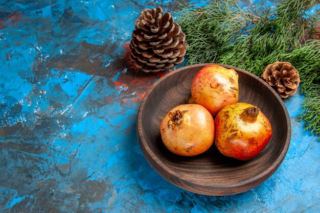 Bovenaanzicht granaatappels op houten plaat dennenboomtak en kegels op blauwe achtergrond