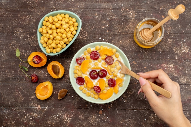 Bovenaanzicht granen met melk in plaat met vers fruit mengen door vrouw op hout, cornflakes ontbijtgranen