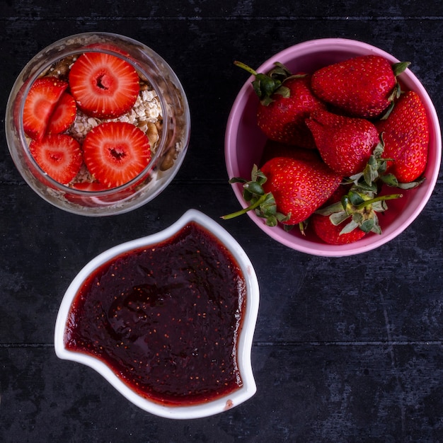 Gratis foto bovenaanzicht granola met fruit en noten in een glas met aardbeien in een roze kom en jam