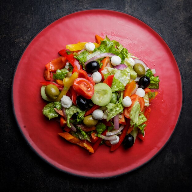 Bovenaanzicht Griekse salade met tomaat en olijven en sla in rode plaat
