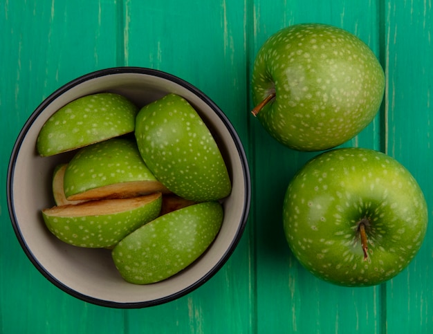 Gratis foto bovenaanzicht groene appelpartjes in kom met geheel op groene achtergrond