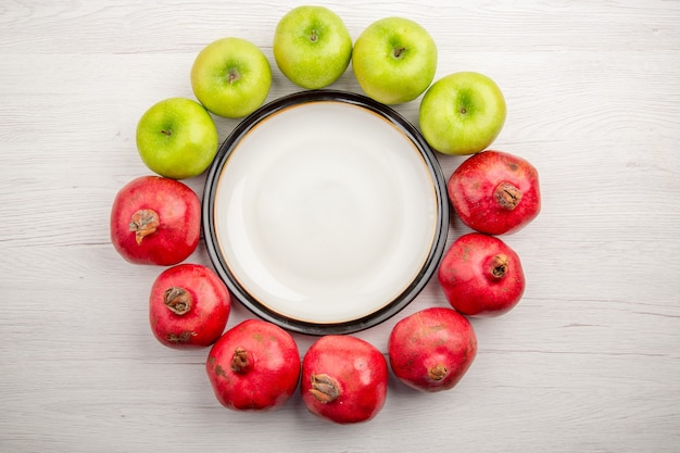 Bovenaanzicht groene appels en granaatappels rond ronde plaat op witte achtergrond