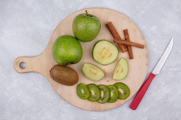 Bovenaanzicht groene appels met kiwi en kaneelplakken op een standaard met een mes op een witte achtergrond