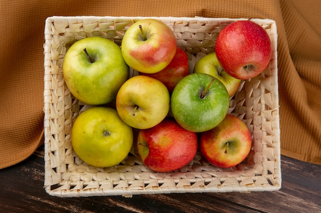 Bovenaanzicht groene en rode appels in een mand op een bruine handdoek op een houten achtergrond