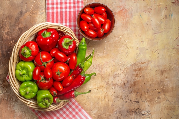 Bovenaanzicht groene en rode paprika's, hete pepers, tomaten in rieten mand, cherrytomaatjes in kom keukenhanddoek op amberkleurige achtergrond