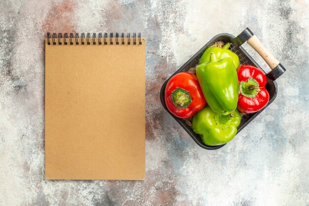 Bovenaanzicht groene en rode paprika's in kom een notitieboekje op naakt oppervlak