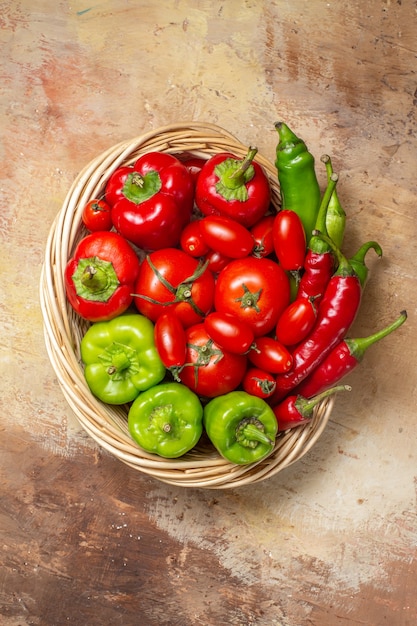 Bovenaanzicht groene en rode pepers hete pepers tomaten in rieten mand op amberkleurige achtergrond