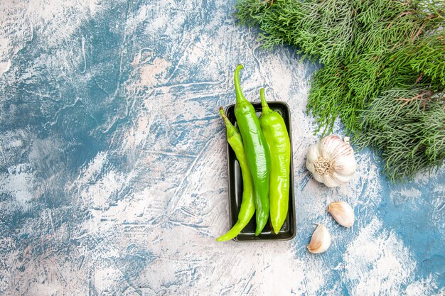 Bovenaanzicht groene hete pepers op zwarte plaat knoflook op blauw-witte achtergrond