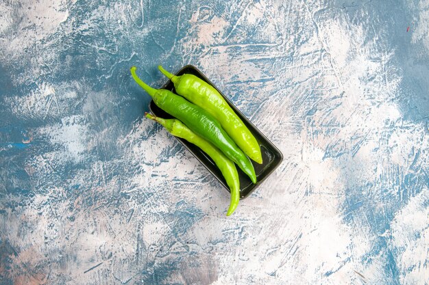 Bovenaanzicht groene hete pepers op zwarte plaat op blauw-witte achtergrond