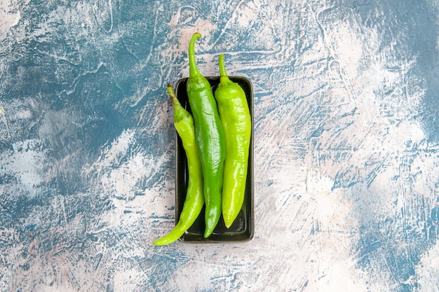 Bovenaanzicht groene hete pepers op zwarte plaat op blauw-witte achtergrond
