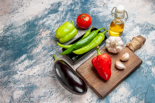 Bovenaanzicht groene hete pepers op zwarte plaat tomaat paprika knoflook op snijplank aubergine op blauw-witte achtergrond