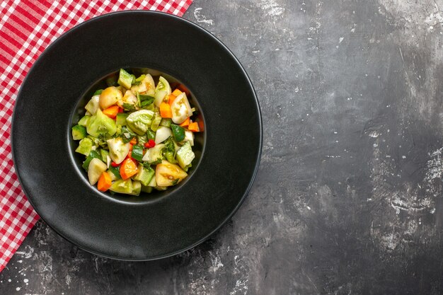 Bovenaanzicht groene tomatensalade op ovaal bord rood tafelkleed op donkere ondergrond