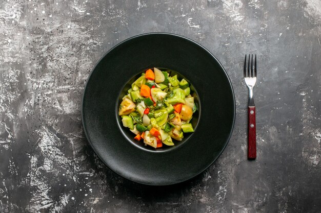 Bovenaanzicht groene tomatensalade op ovale plaat een vork op donkere achtergrond