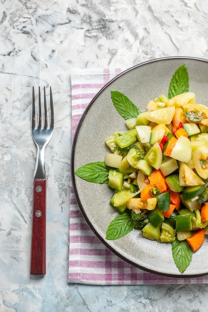 Bovenaanzicht groene tomatensalade op ovale plaat een vork op donkere achtergrond