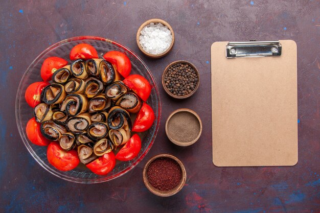 Bovenaanzicht groentemeel gesneden en gerolde tomaten met aubergines en kruiden op de donkere achtergrond