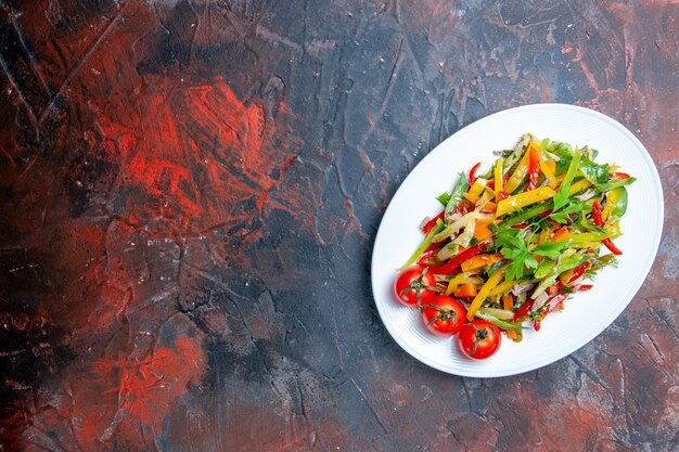 Bovenaanzicht groentesalade op ovale plaat op donkerrode tafel vrije plaats