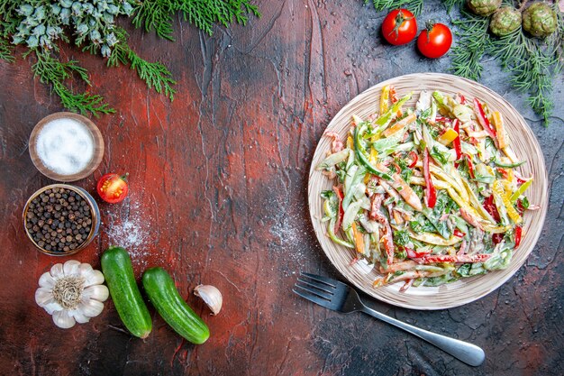 Bovenaanzicht groentesalade op plaat vork tomaten dennentakken komkommers knoflook op donkerrode tafel kopie plaats