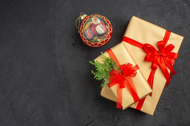 Bovenaanzicht grote en kleine kerstcadeaus in bruin papier gebonden met rood lint kerstbal op donkere achtergrond vrije plaats