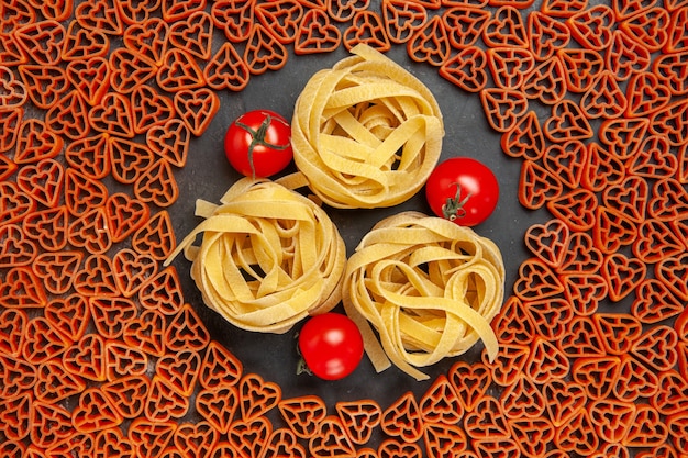 Bovenaanzicht hartvormige Italiaanse pasta tagliatelles en cherrytomaatjes op lege plaats op donkere tafel