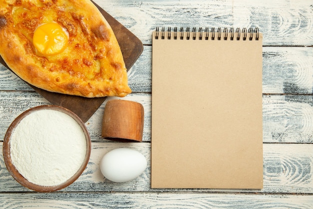 Bovenaanzicht heerlijk eierbrood gebakken met bloem en blocnote op een rustiek bureau