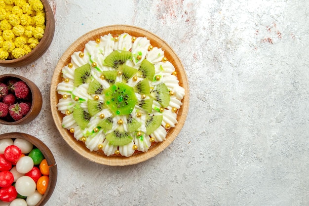 Bovenaanzicht heerlijk kiwi-dessert met snoepjes op lichte witte achtergrond dessert cake crème fruit tropisch